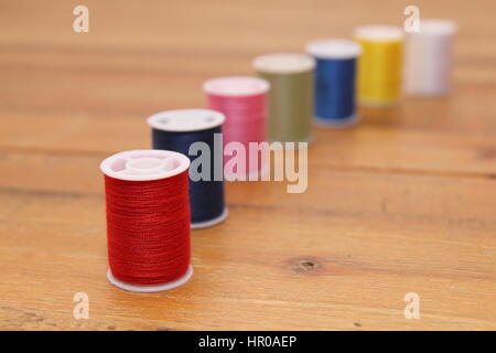 Rangée de bobines de coton multicolores ou bobines sur une table à couture en bois Banque D'Images