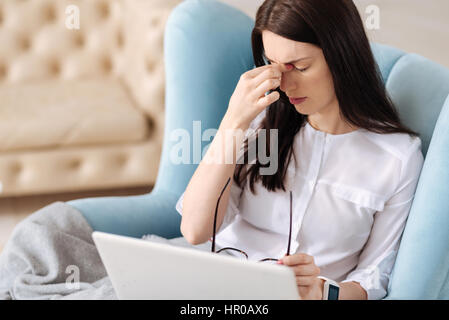 Besoin de se reposer. Malheureux fatigué brunette woman toucher le pont de son nez et holding glasses tout en souffrant des maux de tête Banque D'Images