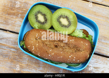 Boîte à lunch saine contenant du fromage brun rouleau et deux moitiés de kiwis Banque D'Images