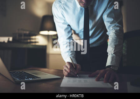 Serious businessman signature au contrat social, travaillant de nuit les heures supplémentaires Banque D'Images