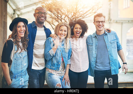 Groupe de beaux jeunes gens dans les modèles (comité permanent près l'un de l'autre bras, posant à l'appareil photo de rire et sourire Banque D'Images