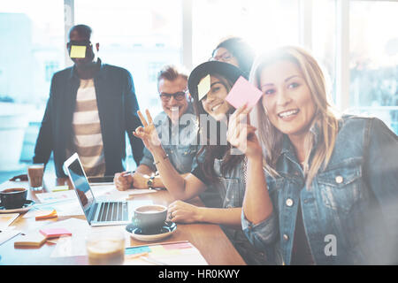 Les jeunes gens magnifiques au cafe table jouant Nom du jeu avec notes autocollant collé à son front posant à l'appareil photo Banque D'Images