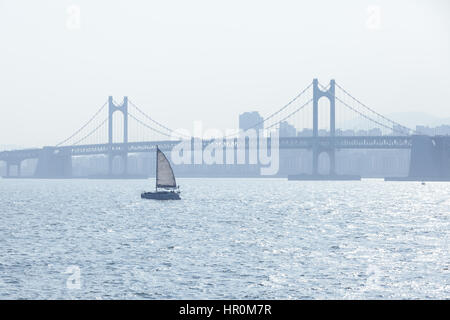 Le yacht navigue à travers le détroit de Corée avec pont Gwangan sur l'arrière-plan, Busan, Corée du Sud. Banque D'Images