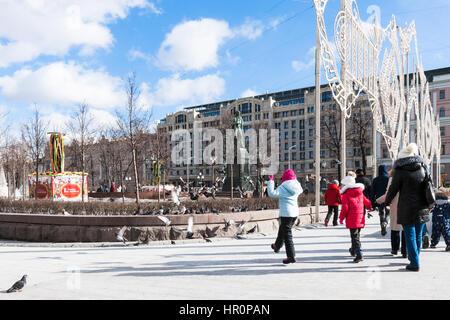 Moscou, Russie. Samedi, 25 février 2017. La place Pouchkine. Méconnaissable, non identifiés les enfants courir après les pigeons. Monument de la poète russe Alexandre Pouchkine en arrière-plan. Journée ensoleillée à Moscou, mais encore froid à température -1C (30F). Inondé de soleil rénové et restauré des rues et places de la grande ville. Mélange d'anciens et de nouveaux styles de l'architecture et les styles de vie. Banque D'Images
