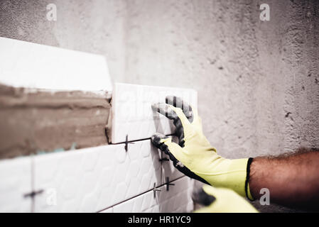 Travailleur industriel, placer de petits carreaux de céramique avec entretoise en plastique sur les murs de salle de bains Banque D'Images