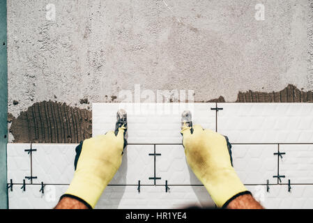 Travailleur industriel, un homme à l'installation de petits carreaux de céramique sur les murs de salle de bains Banque D'Images
