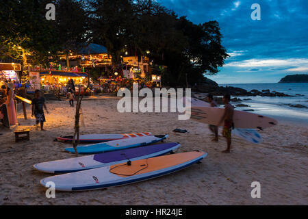 Les surfeurs à pied avec des planches de surf au coucher du soleil sur la plage de Kata, à Phuket, Thaïlande Banque D'Images