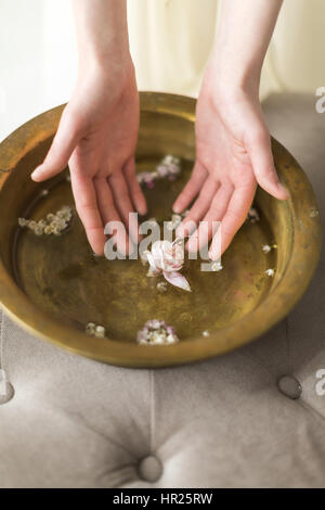 Mains de la jeune fille effleurer la belle fleur rose doucement flotter dans l'eau dans un vase vintage. Le Spa intérieur, des bacs pour mains Banque D'Images