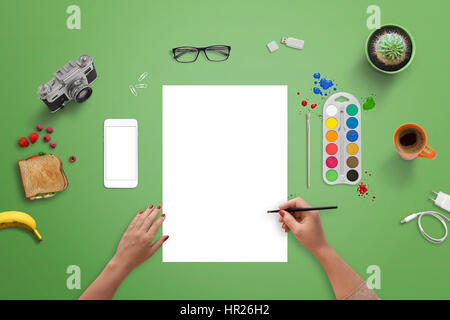 Girl painting sur un papier blanc vierge avec un pinceau et des couleurs de l'eau. Vue de dessus de bureau vert. Banque D'Images
