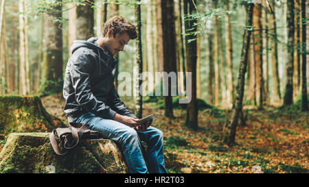 Beau jeune homme assis dans les bois et à l'aide d'un écran tactile numérique, connexion wi-fi et la liberté concept Banque D'Images