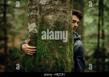 Jeune homme se détendre dans la forêt et s'étreindre un arbre couvert de mousse Banque D'Images
