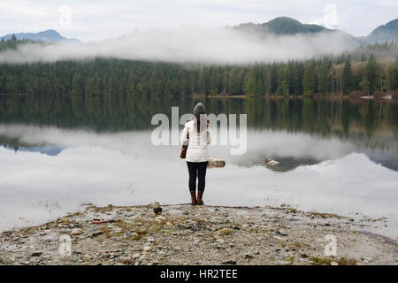 Une femme est au bord de la lac couvert de brume dans Davis Lake Provincial Park, près de la ville de Mission, en Colombie-Britannique, Canada. Banque D'Images