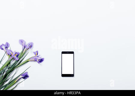 Bouquet de violette iris et téléphone mobile sur un tableau blanc Vue de dessus, copy space Banque D'Images