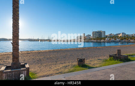 La fin de l'après-midi soleil tombe sur la plage, de la marina et de la promenade. St Antoni de Portmany, Ibiza, Espagne. Plage vide et l'eau calme comme soirée approche. Banque D'Images