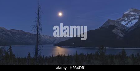 Pleine Lune au-dessus du lac Minnewanka Blue Water Reflection nuit ciel panoramique Rocky Mountain Landscape Horizon. Parc national Banff randonnée dans les Rocheuses canadiennes Banque D'Images