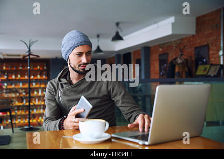 Beau jeune homme hipster avec barbe est à l'aide d'ordinateur dans une cafétéria Banque D'Images