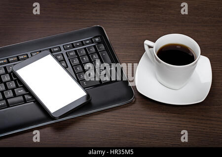 Smartphone moderne avec écran noir, clavier de l'ordinateur et tasse de café sur le bureau en bois foncé 24. Banque D'Images