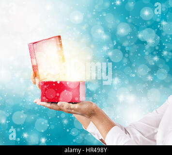 Mains tenant et uverture une boîte cadeau rouge avec effets spéciaux magiques lumières. Banque D'Images