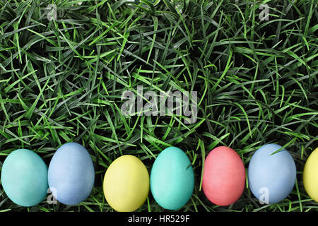 Vue de dessus les oeufs de Pâques colorés alignés dans une rangée sur un fond d'herbe. Mise à plat de style. Banque D'Images