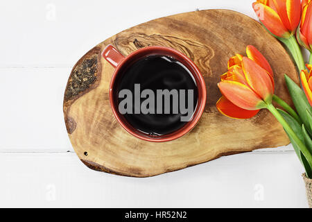 Passage tourné une tasse de café noir fumant avec un bouquet de tulipes orange et jaune fleurs de printemps sur une table en bois blanc dessus. Mise à plat Banque D'Images