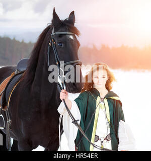 Jeune fille en robe blanche avec des chevaux pur-sang sur le terrain d'hiver. Fond d'équidés historique Banque D'Images