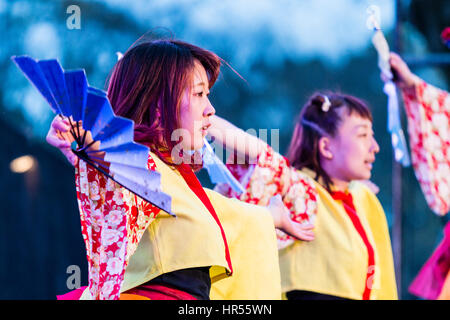 Danse Yosakoi Festival. Deux jeunes danseurs en yukata femme jaune vestes et manches longues, holding open fans en dansant sur scène. En soirée. Close up. Banque D'Images