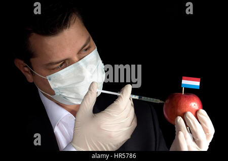 Jeune homme d'injection de produits chimiques dans un apple avec Luxembourg drapeau sur fond noir Banque D'Images