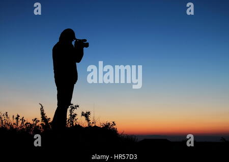 Silhouette d'homme debout dans le coucher du soleil sur la montagne avec caméscope Banque D'Images