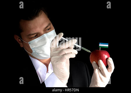 Jeune homme d'injection de produits chimiques dans un apple avec l'Ouzbékistan drapeau sur fond noir Banque D'Images