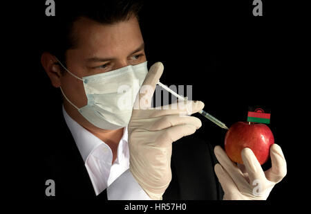 Jeune homme d'injection de produits chimiques dans un apple avec le Malawi drapeau sur fond noir Banque D'Images