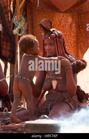 Une mère Himba joue avec son fils alors qu'il était assis à l'extérieur dans une zone proche de un pot cuire sur le feu. Banque D'Images