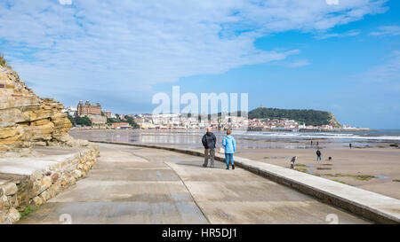 Mature couple marchant le long de la promenade à Scarborough, une station balnéaire populaire sur la côte de North Yorkshire, Angleterre. Banque D'Images