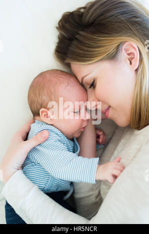 Belle jeune mère avec son nouveau-né fils couché sur lit dans sa chambre en souriant. Banque D'Images