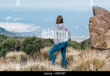 Jeune femme à la scène à plus de nuages à partir du bord de la colline, vue arrière Banque D'Images