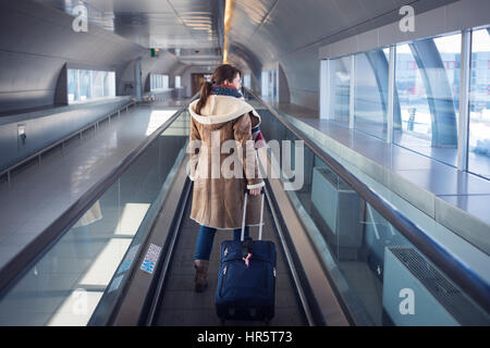 Jeune femme dans l'aéroport portant une valise sur le tapis roulant à la porte de l'avion Banque D'Images