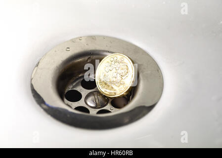 Seul British Pound Coin resting in a silver plughole avec gouttelettes d'eau sur le coin et blanc céramique Banque D'Images