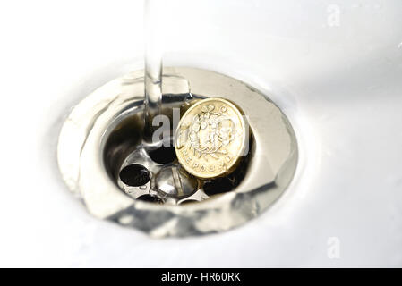 Seul British Pound Coin resting in a silver plughole avec gouttelettes d'eau sur le coin et blanc céramique Banque D'Images