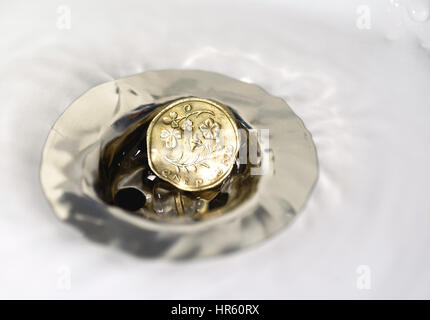 Seul British Pound Coin resting in a silver plughole avec gouttelettes d'eau sur le coin et blanc céramique Banque D'Images