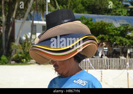 L'homme est la vente de chapeaux sur une plage sur l'île de Boracay. Beaucoup de chapeaux sur sa tête. protection contre le soleil chaud. Banque D'Images