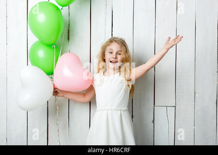 Peu joyeuse fille blonde avec des ballons sur fond de bois blanc. Banque D'Images