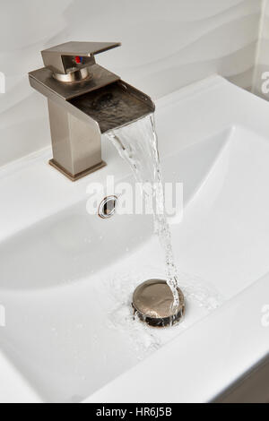 L'eau courante de robinet nickel brossé sur le dessus de la vanité moderne blanc et lavabo en marbre. Banque D'Images