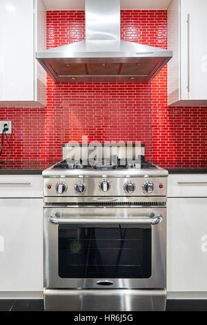 Cuisine moderne avec armoires blanc, red back splash, inox four et hotte. Banque D'Images