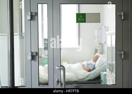 Plan large image de porte en verre en clinique avec green autocollant sur sa fermeture avec clé de verrouillage, senior patient dormir sur le lit à l'intérieur Banque D'Images