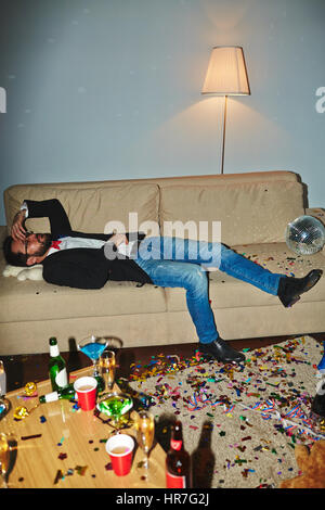Asian man in lunettes ayant terrible gueule de bois : il allongé sur table en salle malpropre et toucher la tête endoloris Banque D'Images
