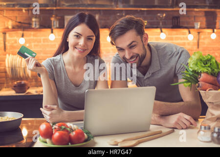 Commande en ligne. Couple dans la commande en ligne de l'alimentation cuisine restaurant. Ils en utilisant l'ordinateur portable. Woman looking at camera et souriant tout en payant avec cr Banque D'Images