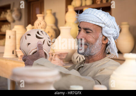 Muscat, Oman - Dec 4, 2017 : Un vieil homme omanais dans une robe traditionnelle montrant outre de ses poteries. Banque D'Images