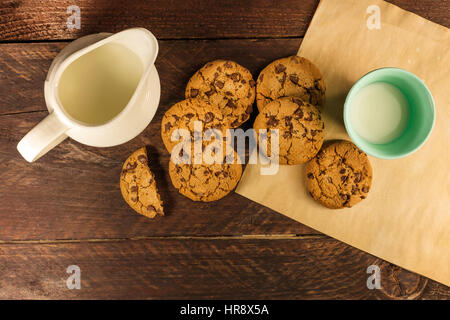 Une photo prise à la verticale de chocolat cookies sur du papier sulfurisé, avec un pot et un verre de lait, et l'espace de copie Banque D'Images