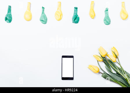 Tulipes jaunes, d'un téléphone mobile, et les ballons sur un tableau blanc, vue du dessus Banque D'Images