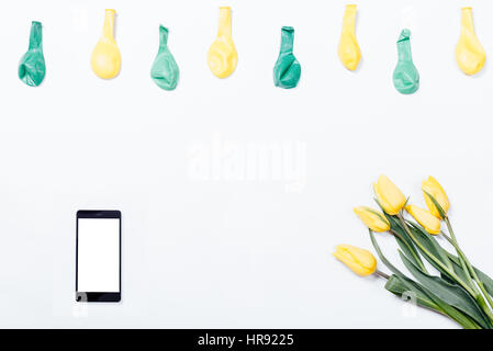 Fleurs jaunes, d'un téléphone mobile, et les ballons sur un tableau blanc, vue du dessus Banque D'Images