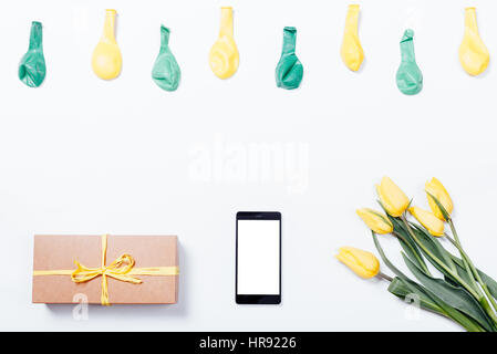 Fleurs jaunes, d'un téléphone mobile, boîte-cadeau avec un ruban et des ballons sur un tableau blanc, vue du dessus Banque D'Images